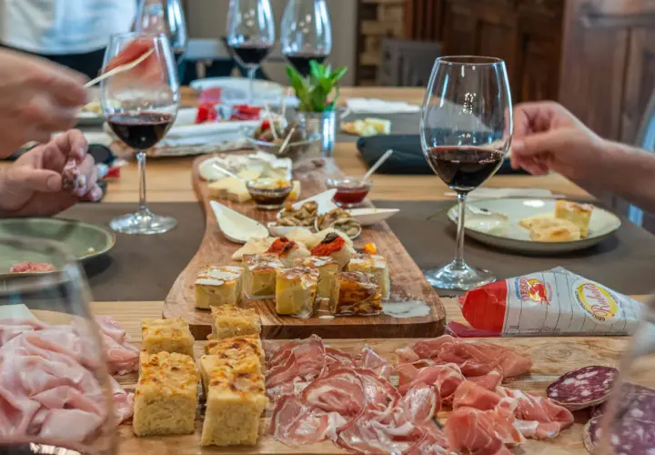 Un tavolo imbandito per una degustazione enogastronomica: salumi, formaggi, focacce e vino rosso invitano a un'esperienza di sapori.