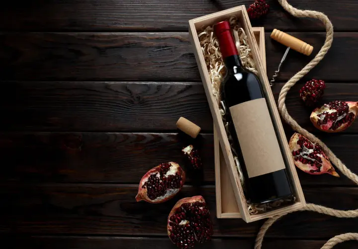 Scatola di legno con bottiglia di vino rosso, melograni e cavatappi, evocando i vini tipici della Campania.