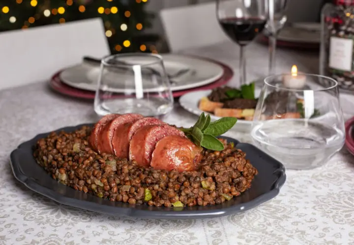 Piatto di cotechino affettato su lenticchie, pronto per essere gustato con un buon vino da abbinare al cotechino.
