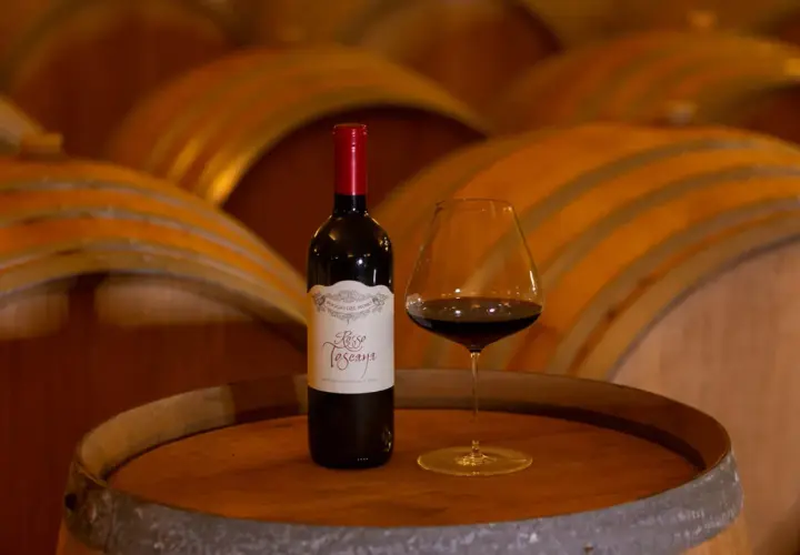 Bottiglia e calice di vino rosso su una botte, con botti di legno sullo sfondo. Un assaggio del governo toscano vino.