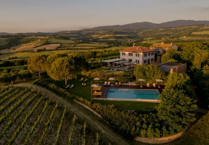 Un incantevole wine resort in Umbria, con vigneti rigogliosi, una piscina scintillante e colline ondulate al tramonto.