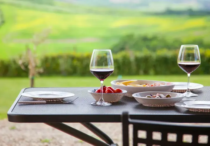 Un bicchiere di Chianti Classico, pomodorini e formaggi su un tavolo all'aperto, con un paesaggio verde sullo sfondo.