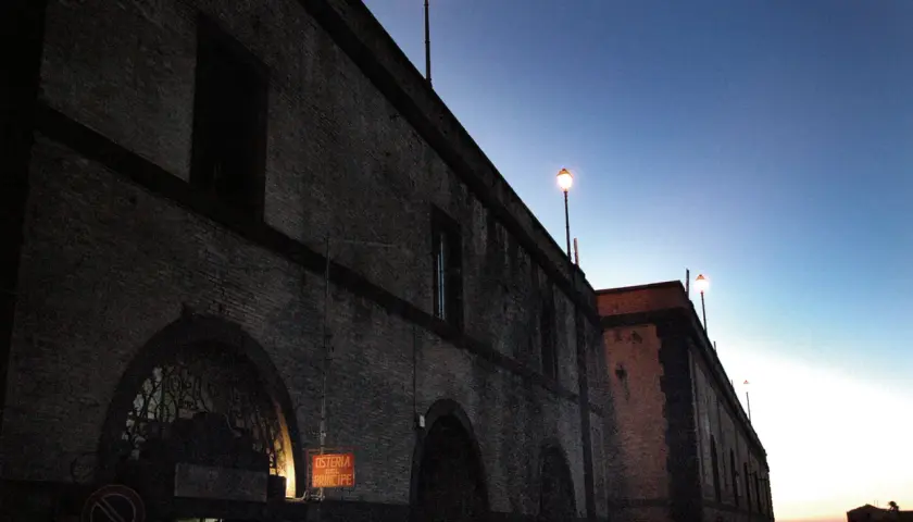 Edificio in mattoni con lampioni accesi al crepuscolo. L'insegna "Osteria del Principe" evoca il **frasca significato** di un luogo conviviale.