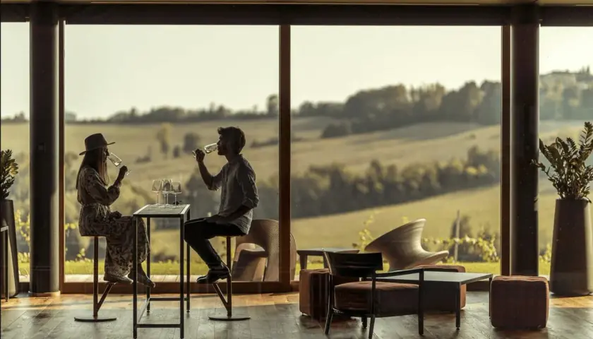 Coppia degusta vino in un'elegante sala con vista sulle colline. Un'esperienza di cantine con pernottamento in Piemonte.