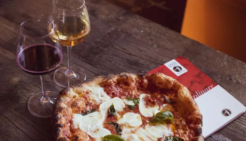 Una pizza fumante con mozzarella e basilico, accompagnata da calici di vino rosso e bianco, perfetti per un'ottima pizza.