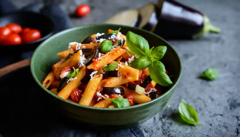 Piatto di pasta alla norma con melanzane, pomodoro e basilico, perfetto per un abbinamento vino.