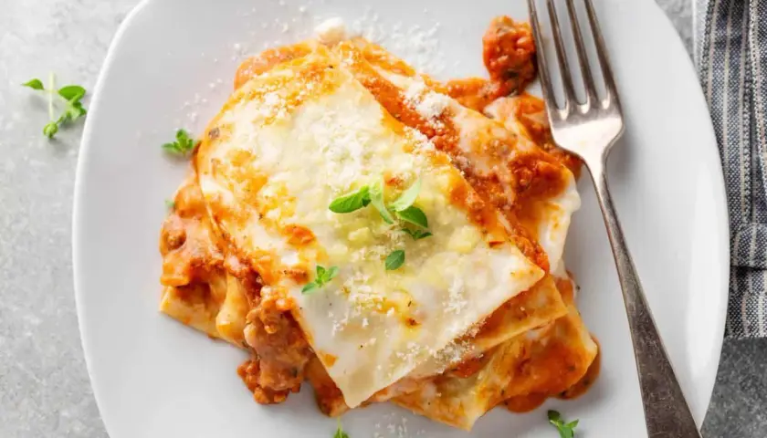 Porzione di lasagne al ragù, ricca e fumante, con besciamella e parmigiano. Perfetta con un buon vino per lasagne.
