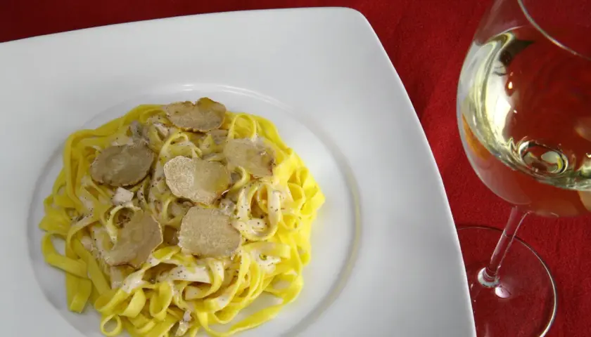 Tagliatelle con crema e scaglie di tartufo bianco, accanto un calice di vino da abbinare al tartufo bianco.