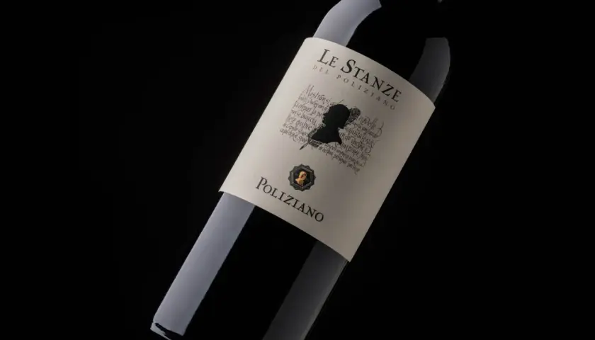 Bottiglia di vino rosso "Le Stanze del Poliziano" su sfondo nero. L'etichetta presenta un profilo silhouette e testo calligrafico.