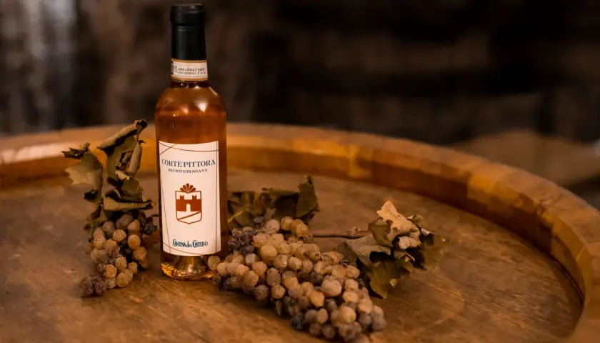 Bottiglia di Recioto di Soave con uva appassita e foglie secche, suggerendo i suoi abbinamenti.