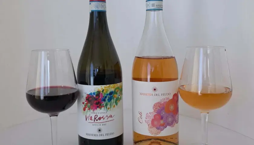 Due bottiglie di vino, una rossa e una rosata, con i loro calici. La **Masseria del Feudo** presenta le sue etichette colorate.