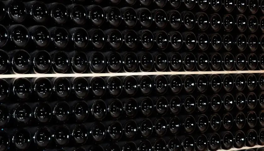 Fila di bottiglie scure, un'immagine che evoca il batonnage cos'è: la tecnica di mescolare il vino in botte per affinarlo.