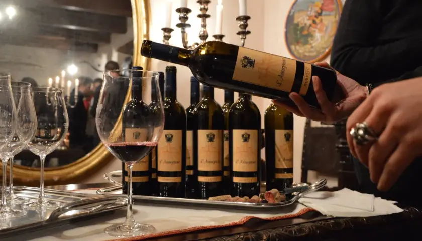 Degustazione di vini delle cantine Goretti: una bottiglia viene versata in un calice, con altre bottiglie e bicchieri su un vassoio.