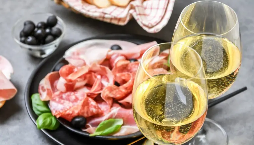 Tagliere di salumi e formaggi con olive, pane e due calici di vino frizzante. Perfetti moscato d'asti abbinamenti per un aperitivo.