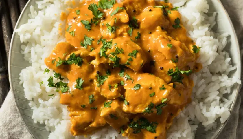 Pollo al curry cremoso su riso bianco, guarnito con prezzemolo fresco. Un vino da abbinare al pollo al curry? Un Gewürztraminer o un Riesling.