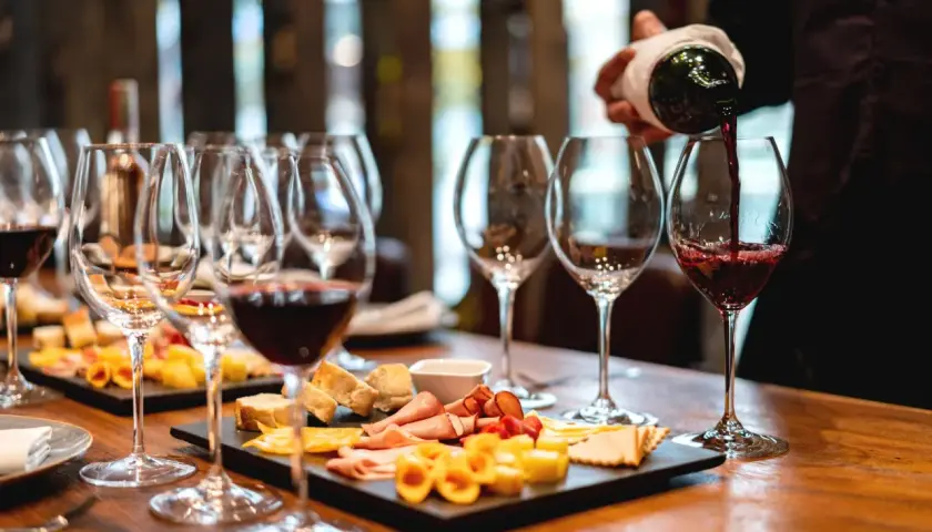 Calice di vino rosso versato, con taglieri di formaggi e salumi. Perfetti abbinamenti per un vino vespaiolo.