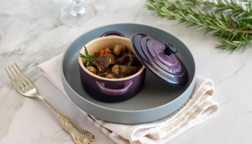 Un saporito stufato di manzo, perfetto per un vino per bourguignonne, servito in una cocotte viola con rosmarino.