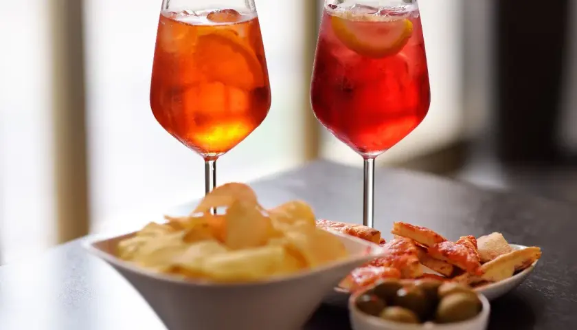 Due cocktail colorati, patatine, olive e pizzette per un romantico aperitivo serale.