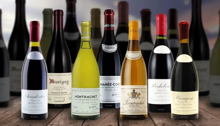 Una selezione di bottiglie costose di vino pregiato, tra cui Montrachet e Musigny, disposte su un tavolo di legno.