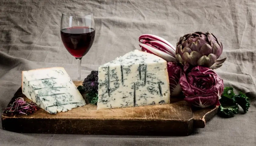 Gorgonzola e vino rosso su tagliere rustico, con radicchio e carciofo. Un perfetto gorgonzola abbinamento vino per un'esperienza gustativa.