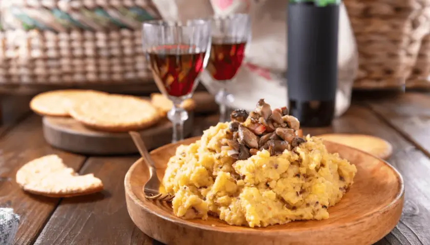 Polenta con funghi, perfetta con un buon vino da abbinare alla polenta. Due calici rossi e una bottiglia completano la scena rustica.