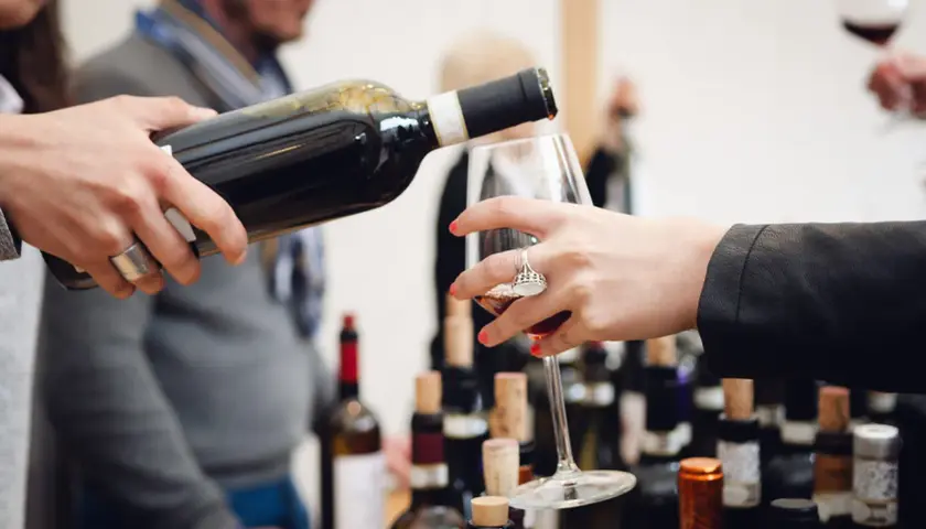 Un bicchiere viene riempito durante una degustazione di Barolo nelle Langhe, tra bottiglie e tappi di sughero.