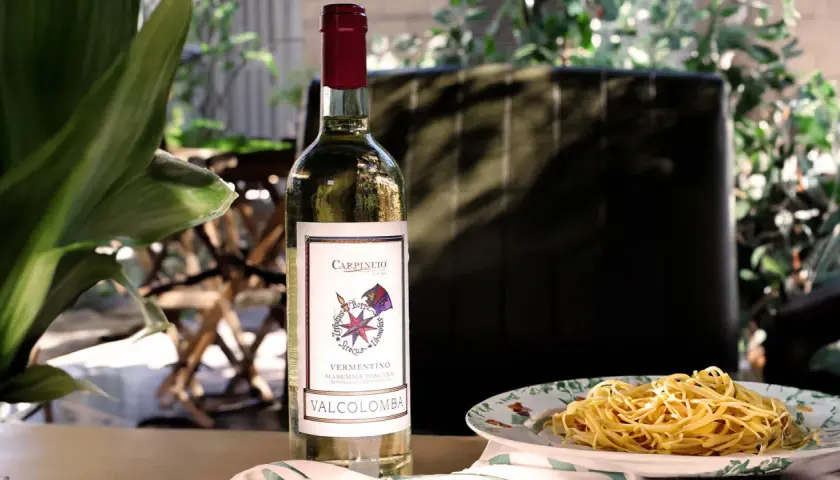 Bottiglia di vino bianco Vermentino Valcolomba, ideale vino per frittura di pesce, accanto a un piatto di spaghetti.