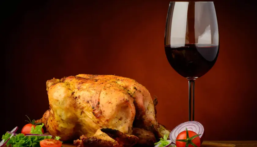 Pollo arrosto dorato con contorno di verdure fresche e un bicchiere di vino rosso, perfetto vino da abbinare al pollo.