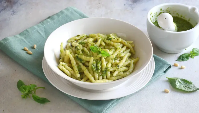 Piatto di trofie al pesto, con mortaio e basilico. Un'idea su cosa abbinare alla pasta al pesto per un pasto fresco e gustoso.