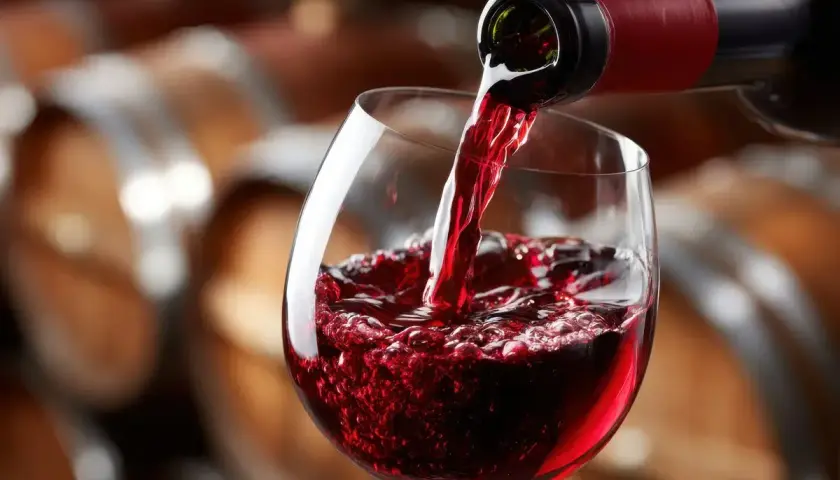 Versando vino rosso in un calice, con botti di legno sullo sfondo. Un sorso di il dolcetto.