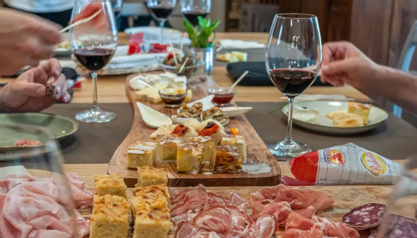 Un tavolo imbandito per una degustazione enogastronomica: salumi, formaggi, focacce e vino rosso invitano a un'esperienza di sapori.