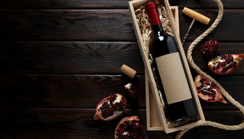 Scatola di legno con bottiglia di vino rosso, melograni e cavatappi, evocando i vini tipici della Campania.