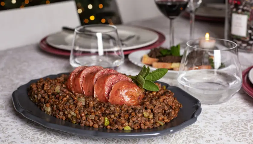 Piatto di cotechino affettato su lenticchie, pronto per essere gustato con un buon vino da abbinare al cotechino.