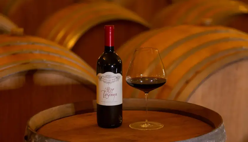 Bottiglia e calice di vino rosso su una botte, con botti di legno sullo sfondo. Un assaggio del governo toscano vino.
