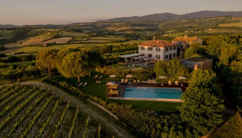 Un incantevole wine resort in Umbria, con vigneti rigogliosi, una piscina scintillante e colline ondulate al tramonto.
