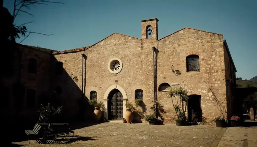 L'abbazia Santa Anastasia, con la sua facciata in pietra e il campanile, si affaccia su un cortile acciottolato.