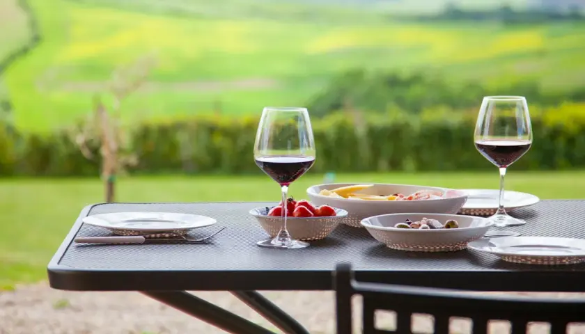 Un bicchiere di Chianti Classico, pomodorini e formaggi su un tavolo all'aperto, con un paesaggio verde sullo sfondo.