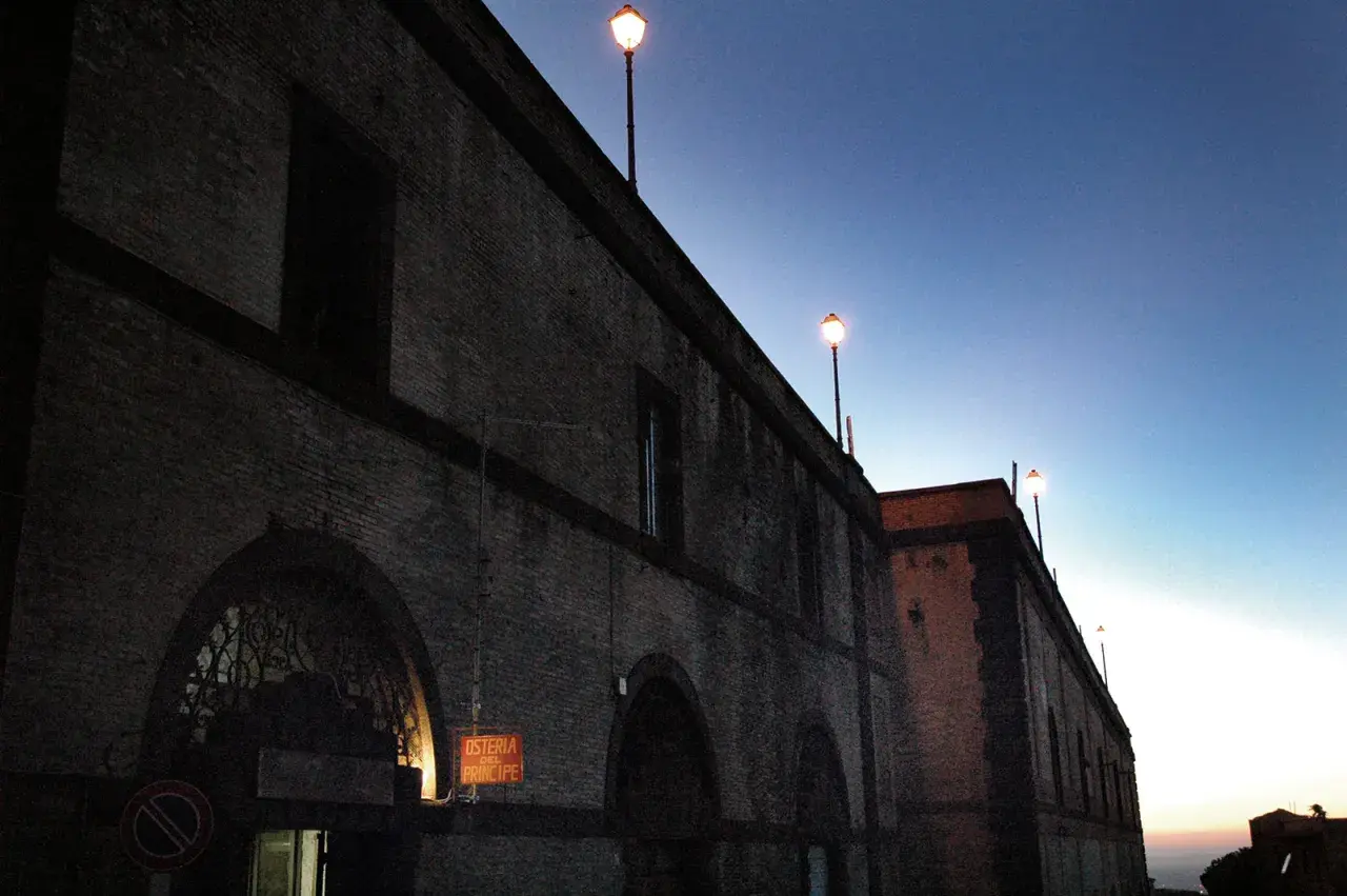 Edificio in mattoni con lampioni accesi al crepuscolo. L'insegna "Osteria del Principe" evoca il **frasca significato** di un luogo conviviale.