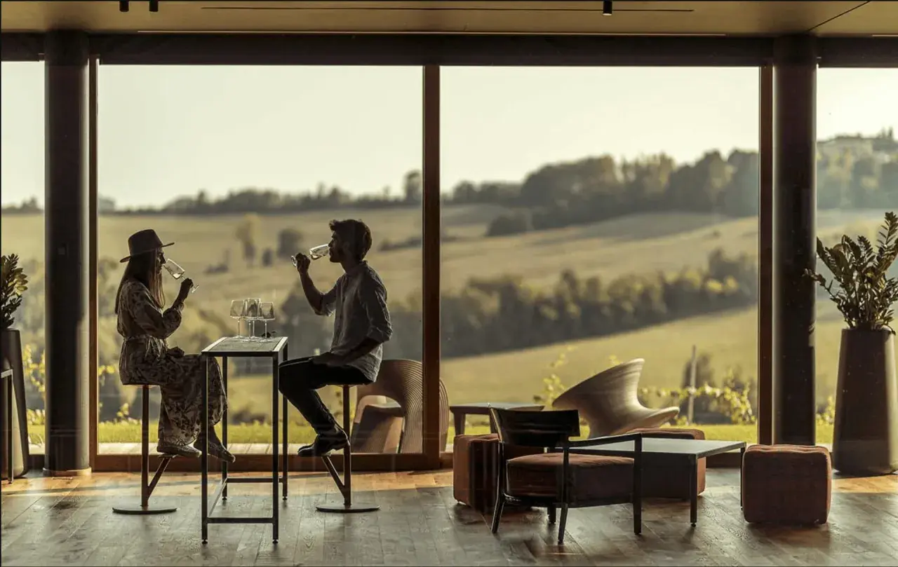 Coppia degusta vino in un'elegante sala con vista sulle colline. Un'esperienza di cantine con pernottamento in Piemonte.
