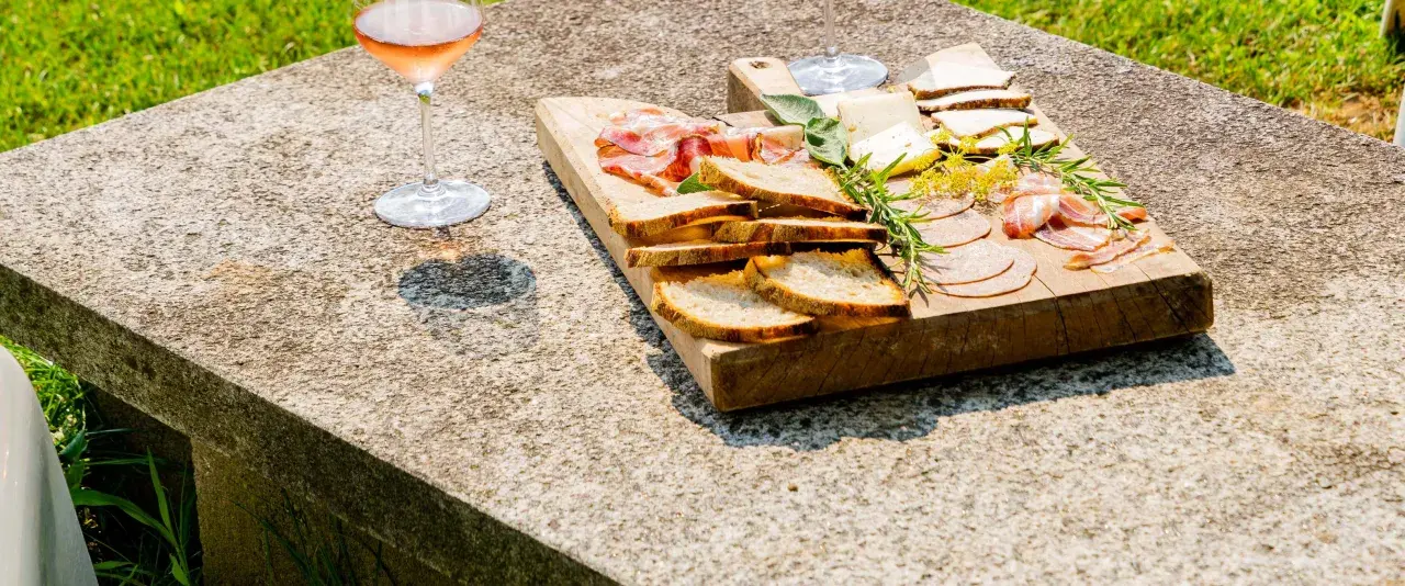 Tagliere di salumi, formaggi e pane, accompagnato da un bicchiere di vino rosato, per una perfetta degustazione vini Piemonte.
