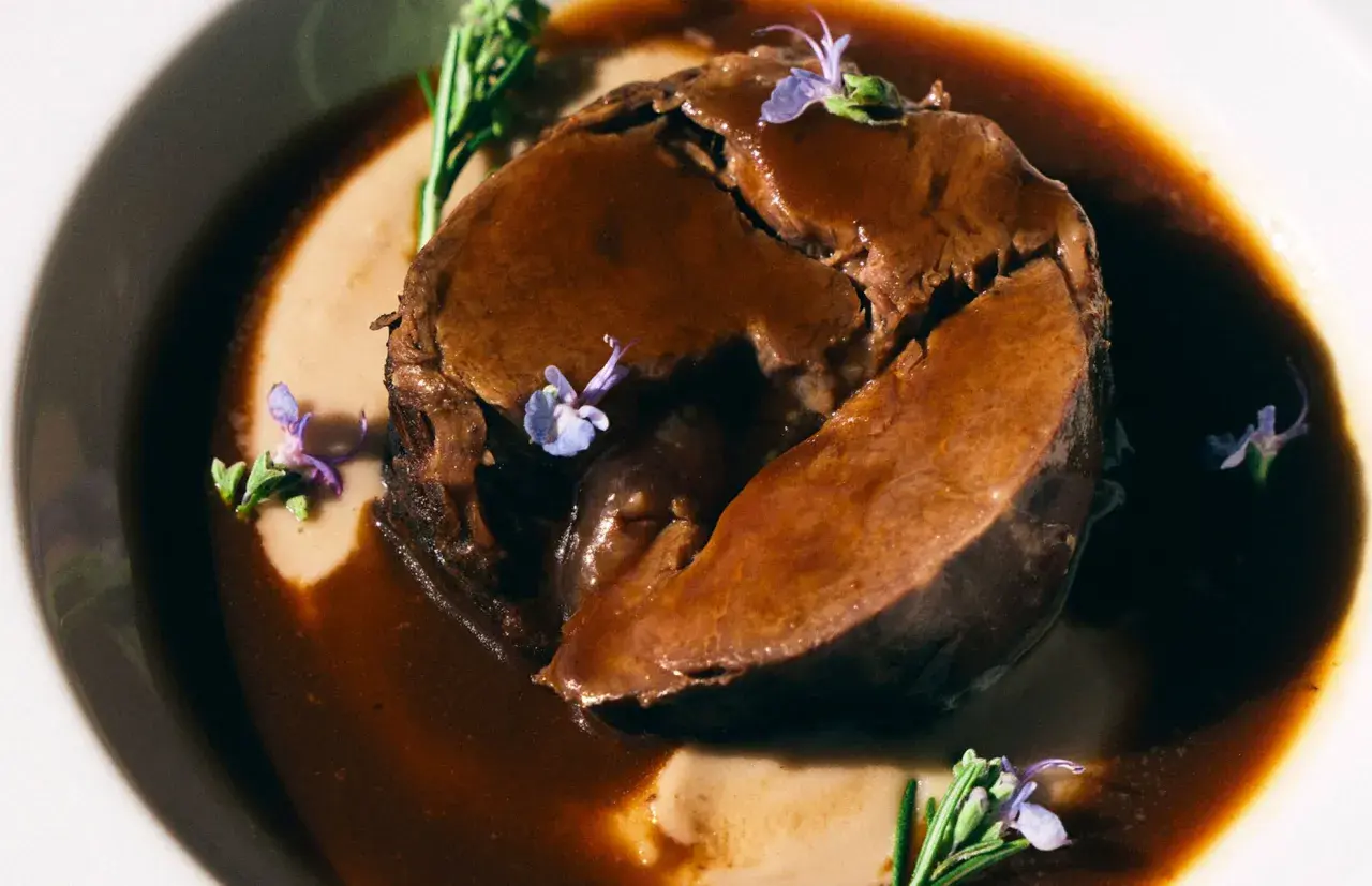 Arrosto succulento in salsa scura, guarnito con rosmarino e fiori viola. Perfetto per i barbera d'asti abbinamenti.