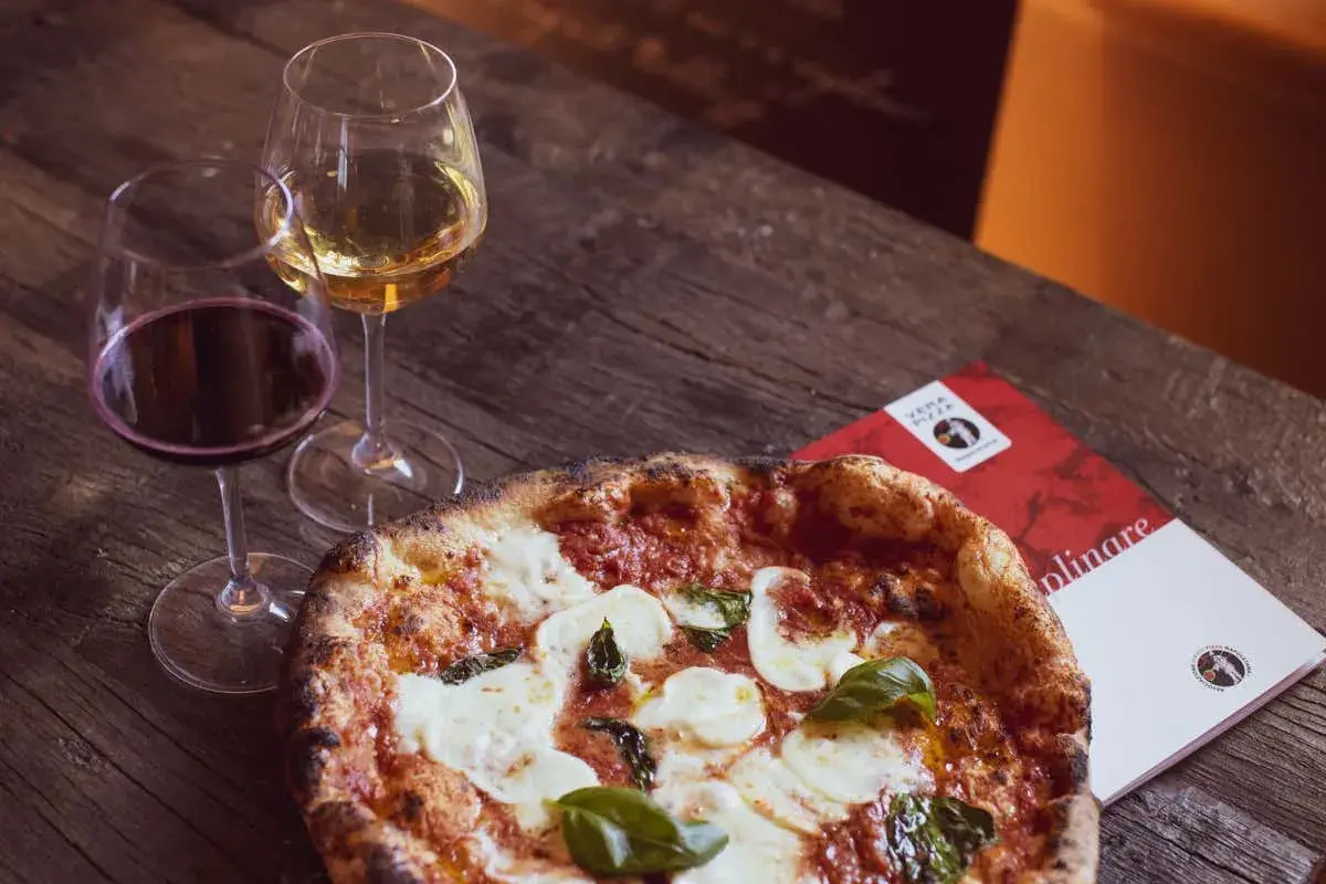 Una pizza fumante con mozzarella e basilico, accompagnata da calici di vino rosso e bianco, perfetti per un'ottima pizza.