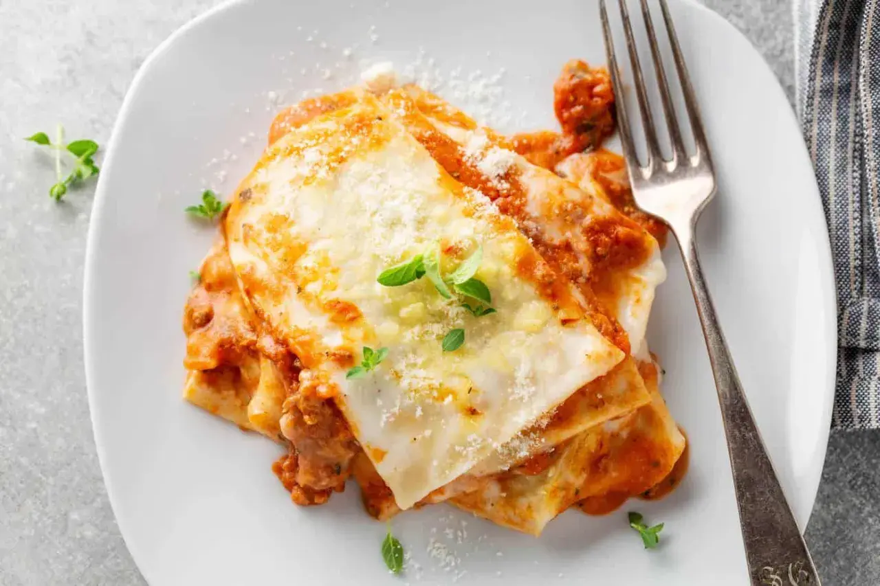 Porzione di lasagne al ragù, ricca e fumante, con besciamella e parmigiano. Perfetta con un buon vino per lasagne.