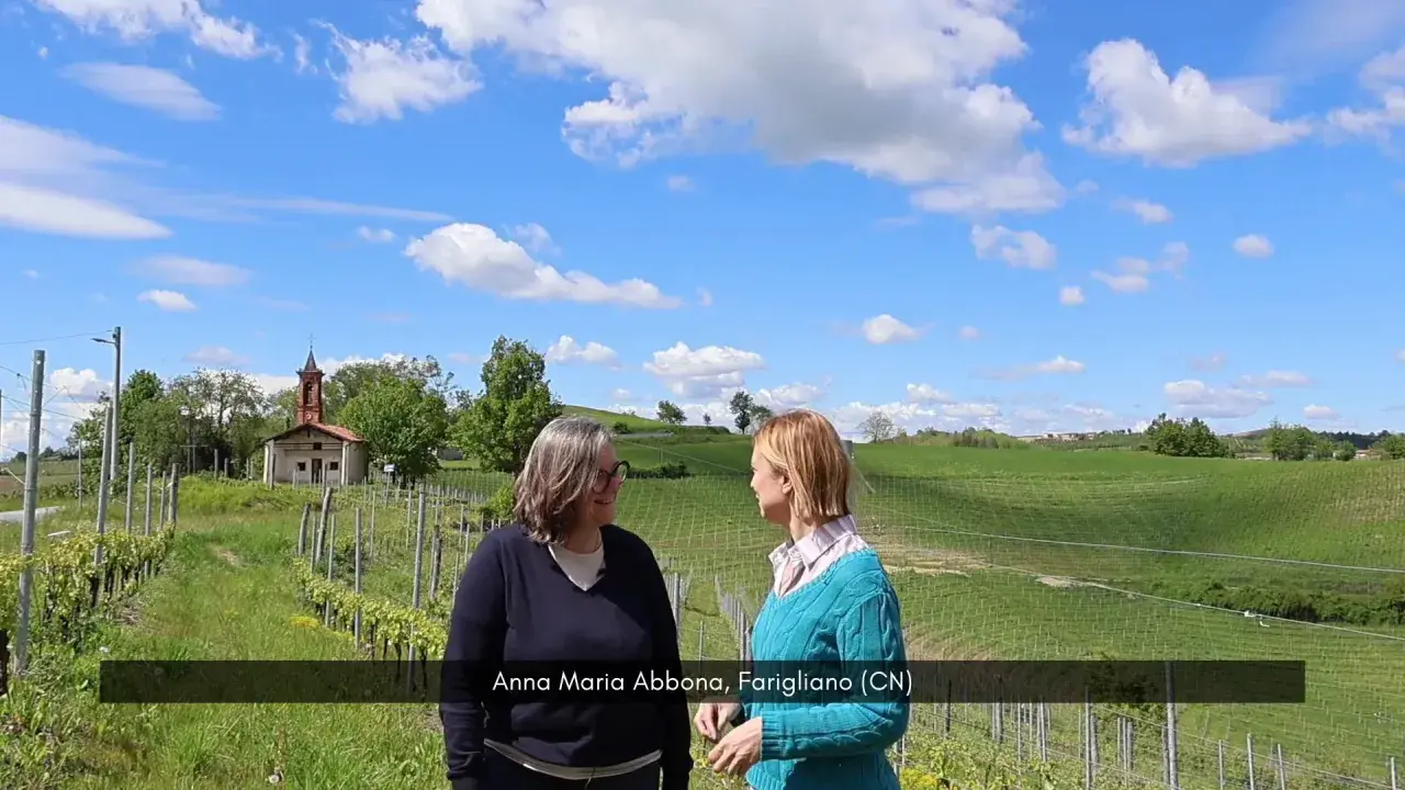 Anna Maria Abbona, della cantina omonima, sorride in un vigneto sotto un cielo azzurro con nuvole bianche.