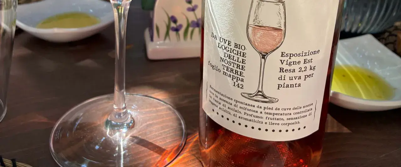 Calice vuoto e bottiglia di vino rosato, pronti per una degustazione vini Sicilia. L'etichetta descrive uve biologiche e note fruttate.