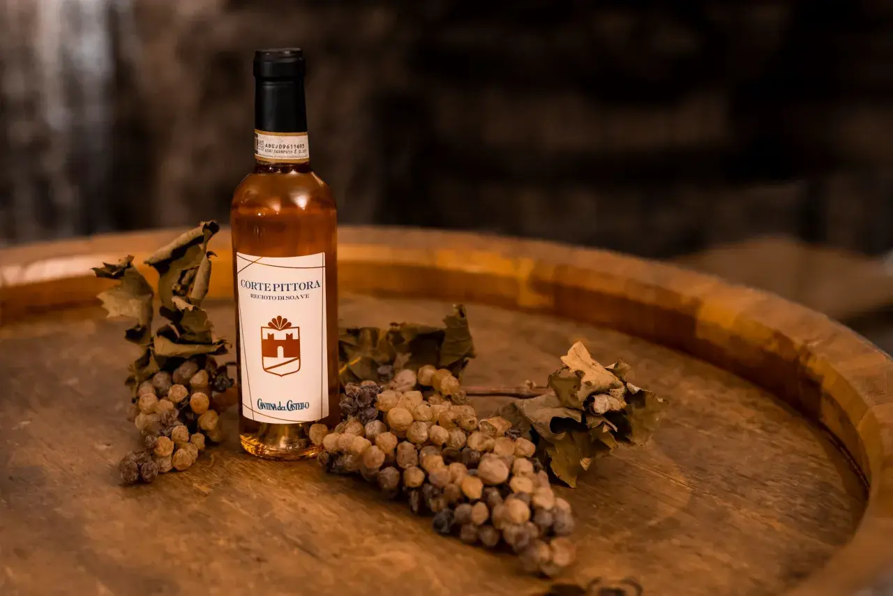 Bottiglia di Recioto di Soave con uva appassita e foglie secche, suggerendo i suoi abbinamenti.