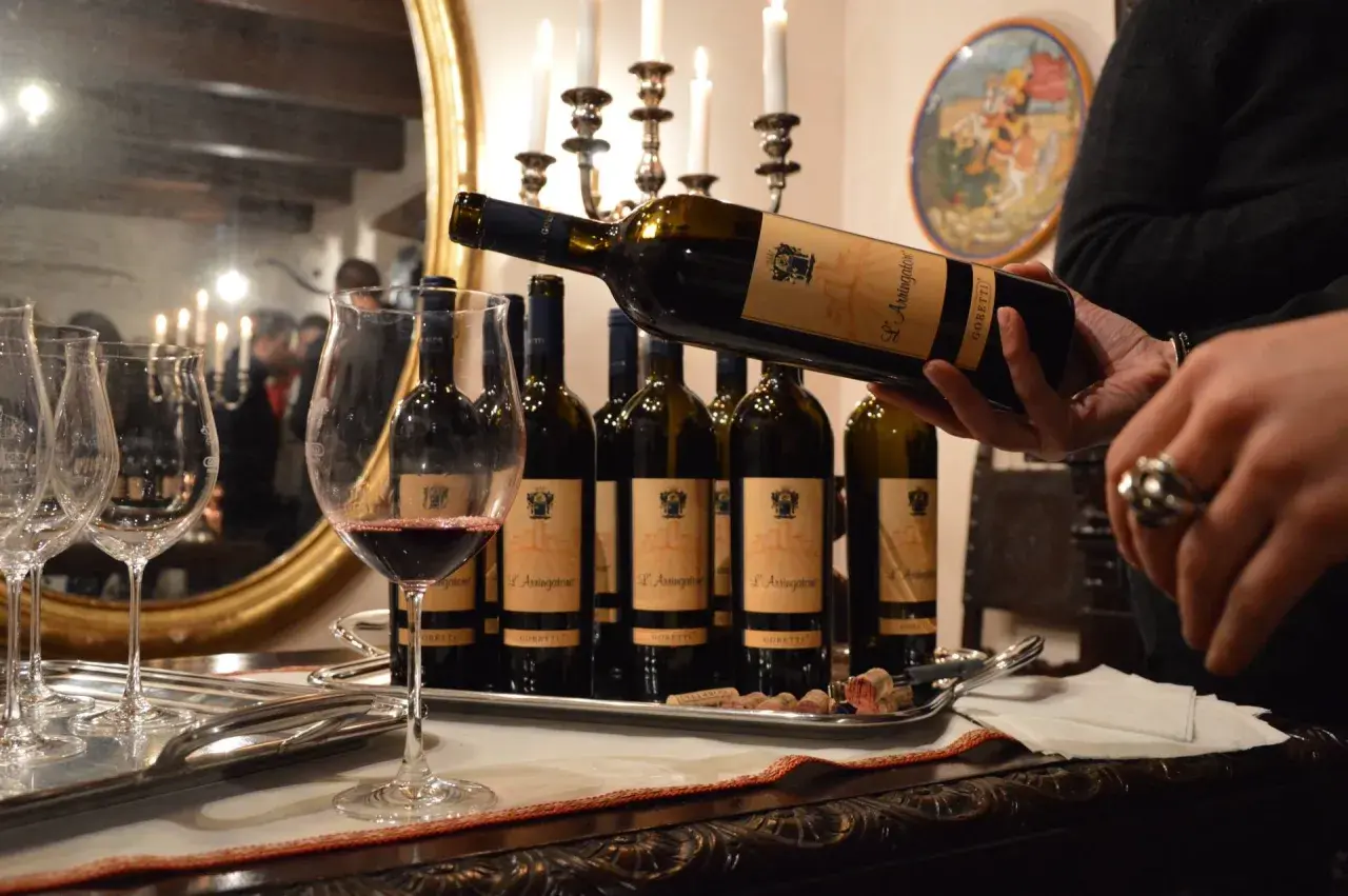 Degustazione di vini delle cantine Goretti: una bottiglia viene versata in un calice, con altre bottiglie e bicchieri su un vassoio.