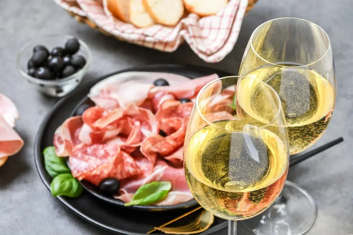 Tagliere di salumi e formaggi con olive, pane e due calici di vino frizzante. Perfetti moscato d'asti abbinamenti per un aperitivo.