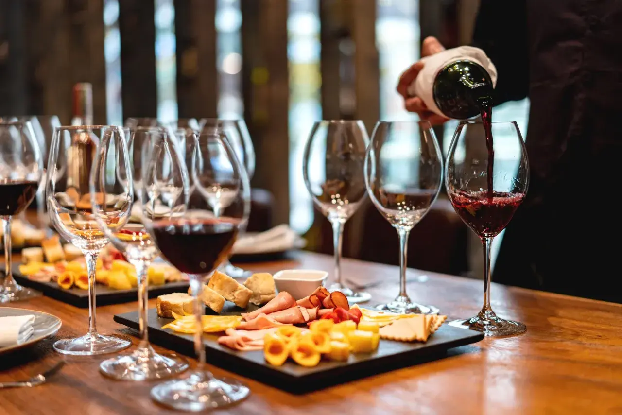 Calice di vino rosso versato, con taglieri di formaggi e salumi. Perfetti abbinamenti per un vino vespaiolo.