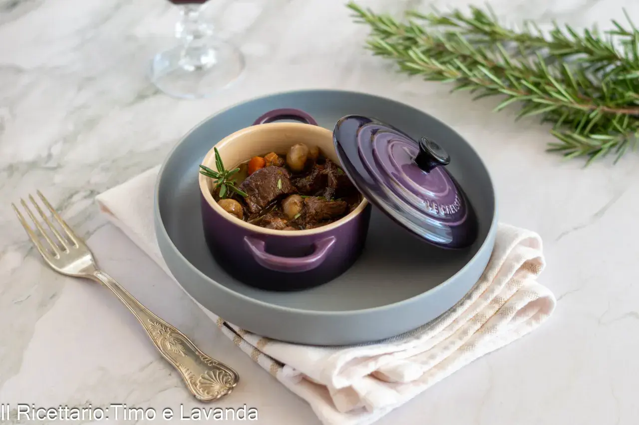 Un saporito stufato di manzo, perfetto per un vino per bourguignonne, servito in una cocotte viola con rosmarino.